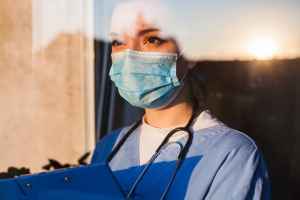 Nurse looking out of window Nurse looking out of a window, wearing a face mask and holding a clip board