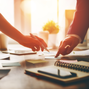 Two people pointing at a post-it note. One pointing whilst holding a pen