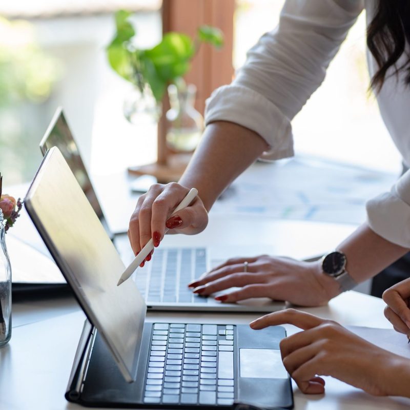 Two people working on a the same laptop Two people gathered around iPad screen. One person using an apple pencil, the other pointing towards the screen